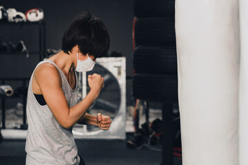 Fototapeta na wymiar woman wearing medical mask training boxing with punching bag in gym