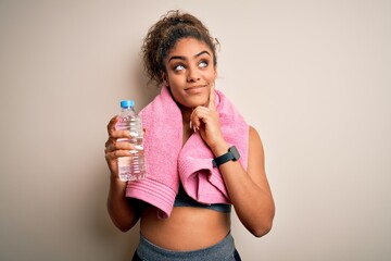 Young african american sporty woman doing sport wearing towel drinking bottle of water serious face thinking about question, very confused idea