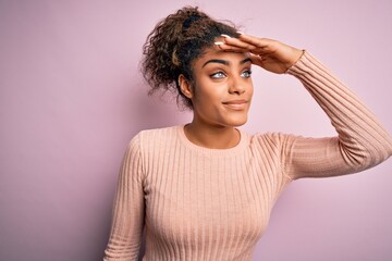 Fototapeta na wymiar Young beautiful african american girl wearing casual sweater standing over pink background very happy and smiling looking far away with hand over head. Searching concept.