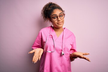 African american nurse girl wearing medical uniform and stethoscope over pink background clueless...