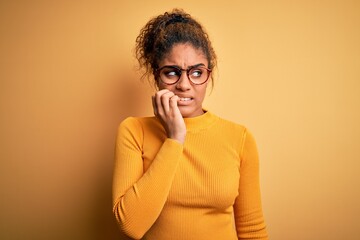 Fototapeta na wymiar Young beautiful african american girl wearing sweater and glasses over yellow background looking stressed and nervous with hands on mouth biting nails. Anxiety problem.