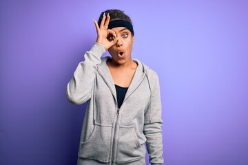 Young african american sportswoman doing sport wearing sportswear over purple background doing ok gesture shocked with surprised face, eye looking through fingers. Unbelieving expression.