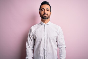 Young handsome man with beard wearing casual shirt standing over pink background Relaxed with serious expression on face. Simple and natural looking at the camera.