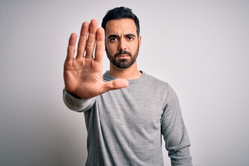 Young handsome man with beard wearing casual sweater standing over white background doing stop sing...