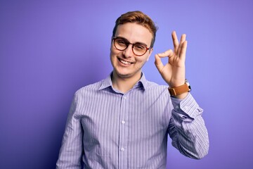 Young handsome redhead man wearing casual shirt and glasses over purple background smiling positive doing ok sign with hand and fingers. Successful expression.