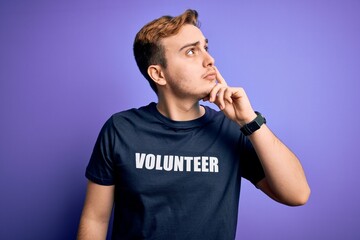 Young handsome redhead man wearing volunteer t-shirt over isolated purple background serious face...
