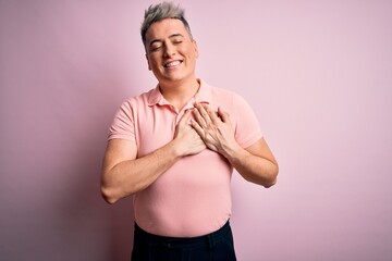 Young handsome modern man wearing casual pink t-shirt over isolated background smiling with hands on chest with closed eyes and grateful gesture on face. Health concept.