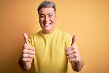 Young handsome modern man wearing yellow shirt over yellow isolated background success sign doing positive gesture with hand, thumbs up smiling and happy. Cheerful expression and winner gesture.