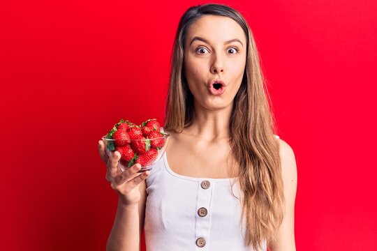 Young beautiful girl holding bowl with strawberries scared and amazed with open mouth for surprise, disbelief face