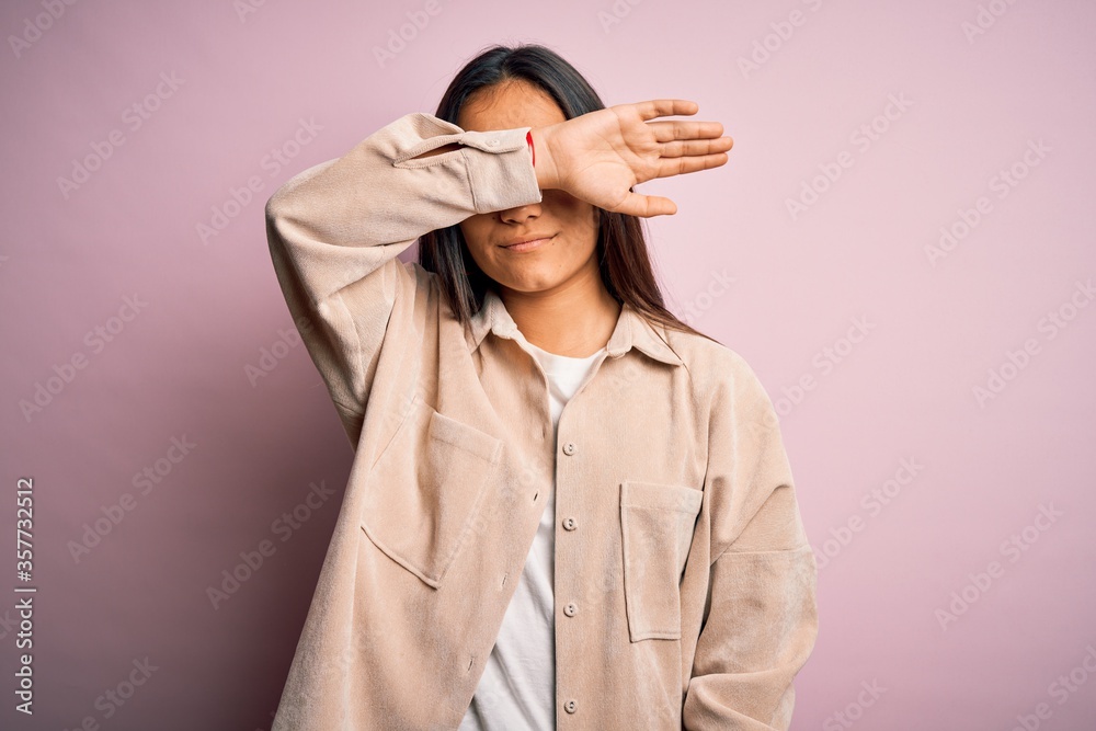 Canvas Prints Young beautiful asian woman wearing casual shirt standing over pink background covering eyes with arm, looking serious and sad. Sightless, hiding and rejection concept