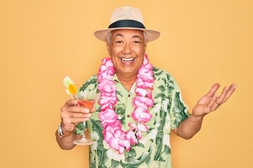 Middle age senior grey-haired man wearing summer hat and hawaiian lei drinking a cocktail very happy and excited, winner expression celebrating victory screaming with big smile and raised hands