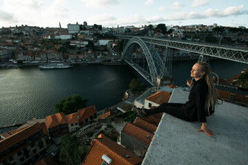 Woman sitting in front of Douro river and Dom luis I bridge in the gloomy weather, Porto, Portugal.