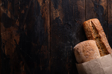 fresh bread in a paper bag on an old wooden background, top view, place for text