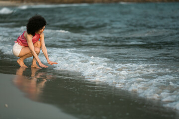 Mixed-race woman kneeling the edge of the surf on the tropical sea beach.