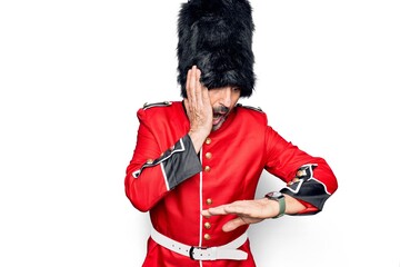 Middle age handsome wales guard man wearing traditional uniform over white background Looking at the watch time worried, afraid of getting late