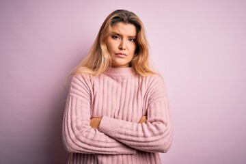 Fototapeta premium Young beautiful blonde woman wearing casual pink sweater over isolated background skeptic and nervous, disapproving expression on face with crossed arms. Negative person.