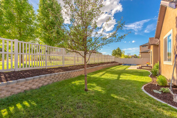 Home backyard with vibrant lawn and raised planting bed along white picket fence