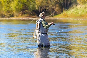 Man fly fishing casting into a river in Autumn