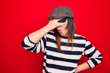 Young beautiful brunette burglar woman wearing cap and mask over isolated red background peeking in shock covering face and eyes with hand, looking through fingers afraid