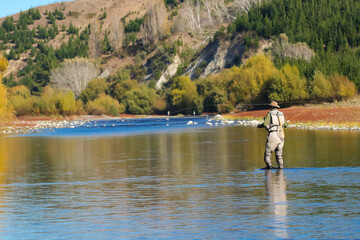 Fototapeta na wymiar Man fly fishing in the distance on a New Zealand river in Autumn