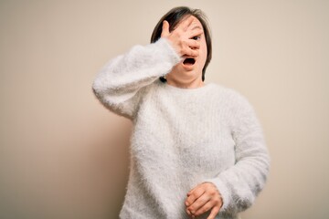 Young down syndrome woman standing over isolated background peeking in shock covering face and eyes...
