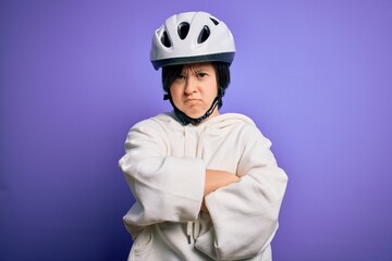 Young down syndrome cyclist woman wearing security bike helmet over purple background skeptic and nervous, disapproving expression on face with crossed arms. Negative person.