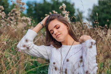 Beautiful brunette teenage girl sitting on the grass, smiling and touching her hair