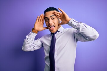Young brazilian businessman wearing elegant tie standing over isolated purple background Smiling cheerful playing peek a boo with hands showing face. Surprised and exited