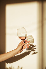 Glass of pink wine in hand with shadow on the wall