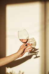 Poster Glass of pink wine in hand with shadow on the wall © valeriyakozoriz