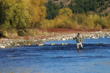 Autumn scenery of fly fisherman in the distance on river rapids