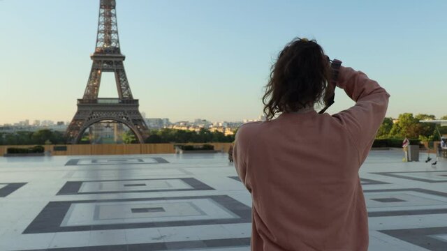 Female photographer taking pictures of the Eiffel tower at the trocadero square in Paris during early summer morning with almost nobody