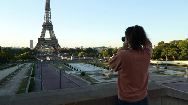 Young woman taking pictures of the eiffel tower with her mirrorless camera during early summer morning in paris France, wide arc shot