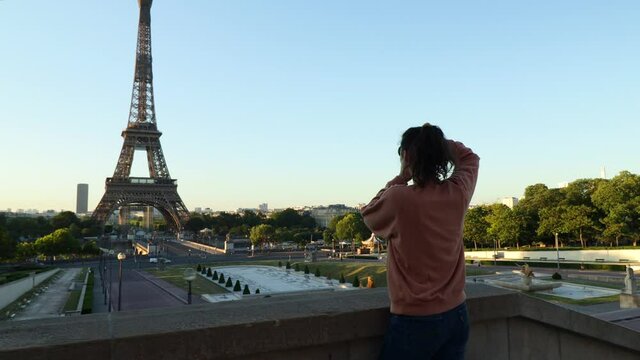 Female photographer taking pictures of the eiffel tower in Paris during early summer morning with her camera, arc wide gimbal shot