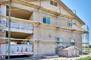 Scaffolds on house under renovations with primer and base coat of stucco mix applied.