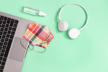 PInk fabric Face Shields and hand sanitizer spray on work place. Flat lay with personal computer and  white headphones on neo mint background with copy space. Top view.