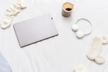 Lazy weekend Morning,  woke up late.  Flat lay with laptop, warm socks, cup of coffee, wireless headphones, mask for sleeping on bed in bedroom.