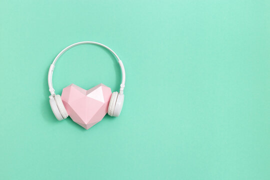 Pink polygonal paper heart shape in white headphones. Music concept. Dj Headset. Minimal style. Mint colored background with copy space.