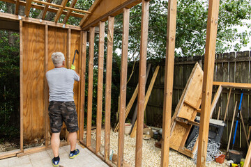 Demolition phase with a man tearing down an old shed with a crowbar in a backyard that was rotting...