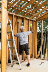 Fototapeta premium Demolition phase with a man tearing down an old shed with a crowbar in a backyard that was rotting and falling apart