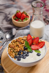Bowl of homemade granola yogurt with fresh berries on wooden board with milk for breakfast