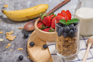 Homemade granola with fresh berries in glass cup on wooden board for breakfast with milk and banana