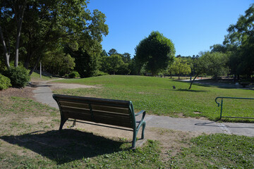 雲一つない青空から夏の陽射しが降り注ぐ広場に、ベンチがある公園の風景