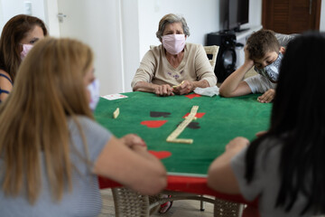 homem, mulher, criança, pessoas usando mascara de proteção e jogando dominó durante a quarentena em casa. Brincando em família. Isolamento social em casa. 