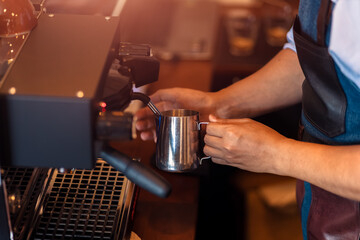Fototapeta na wymiar Barista steaming milk in the pitcher with coffee machine for preparing to make latte art.