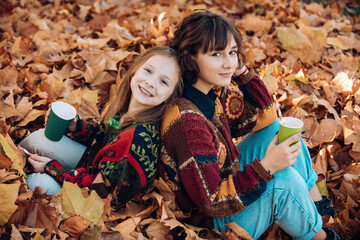 Close up. Autumn girls in autumn park. Sunny fall weather. Beautiful autumn girl with sister in golden park. Happy girls playing with fall leaves in the park.
