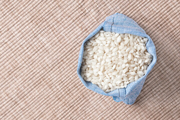 White dry rice in blue pouch on tablecloth. Top view.