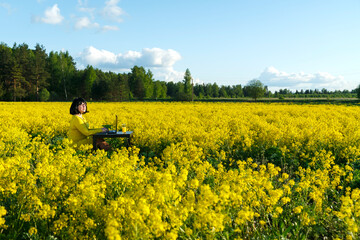 Young woman freelancer in a field among yellow flowers at a table with and a computer.