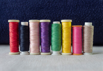 Closeup to a eight multicolor sewing threads over white textile and dark blue background. fashion and textile concept