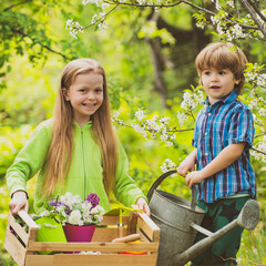Gardening tools and water can for kids. Children planting spring flowers in sunny garden. Little...